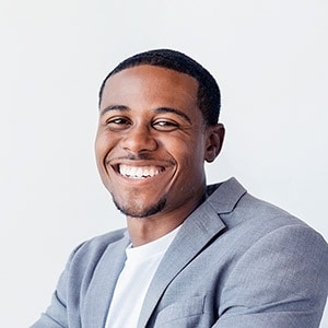 A man with short hair smiles while wearing a light gray blazer and white shirt, against a light background.