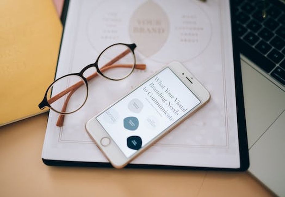 A pair of glasses, a smartphone displaying a website about social media recruitment, a notebook, and a laptop are placed on a desk.