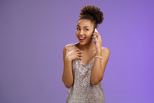 A woman in a sequin dress talks on a phone against a purple background, smiling with her hand on her chest, exemplifying effective customer engagement.