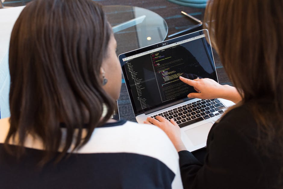 Two people are looking at a laptop screen displaying code, with one person pointing at the screen, discussing user experience (UX) improvements.